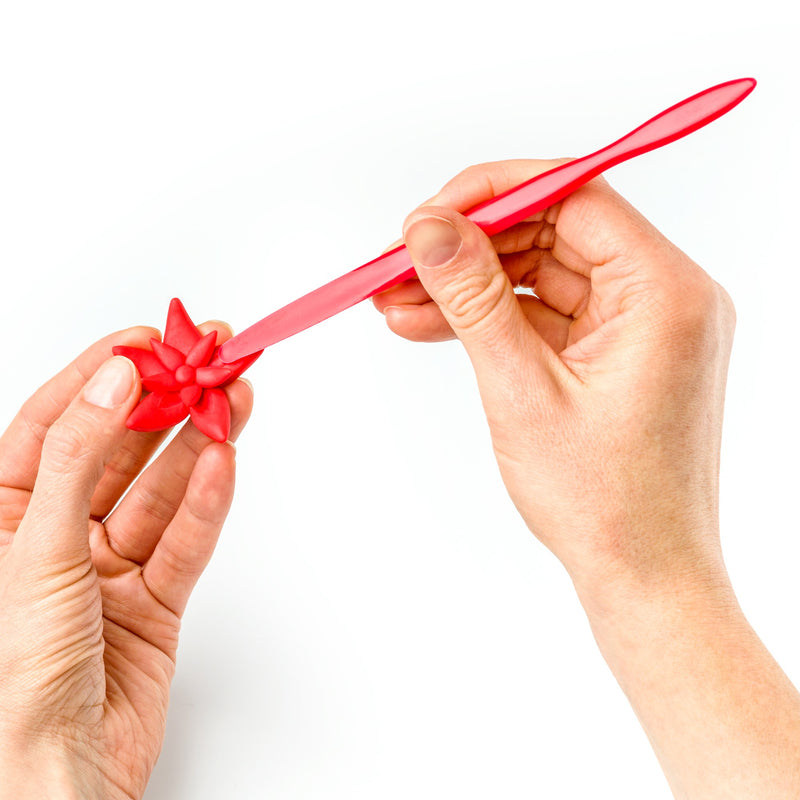 Two hands shaping a red clay flower on the pointed end of a FIMO modelling stick