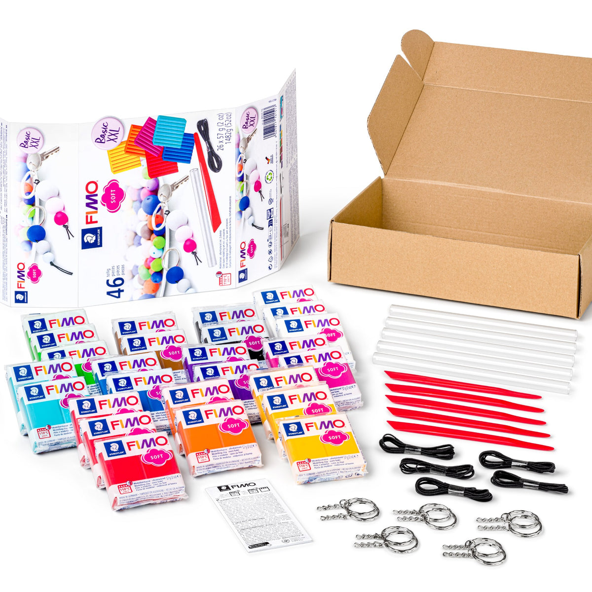 Contents of the FIMO soft Basic XXL set laid out beside the open box: wrapped clay blocks, clear and red modelling tools, black elastic cords, keyrings and an instruction sheet