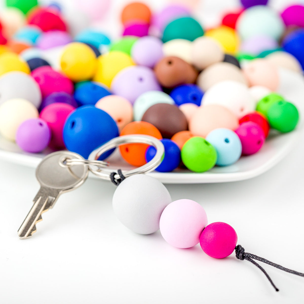 White bowl of round FIMO soft beads in many colours with a key ring of threaded beads in front