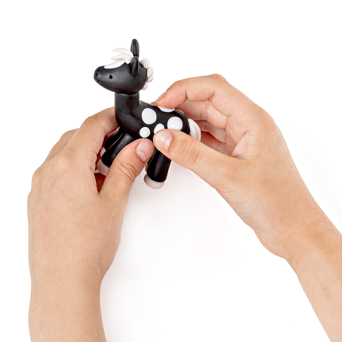 Two hands pressing white spots onto a small black FIMO kids pony during modelling