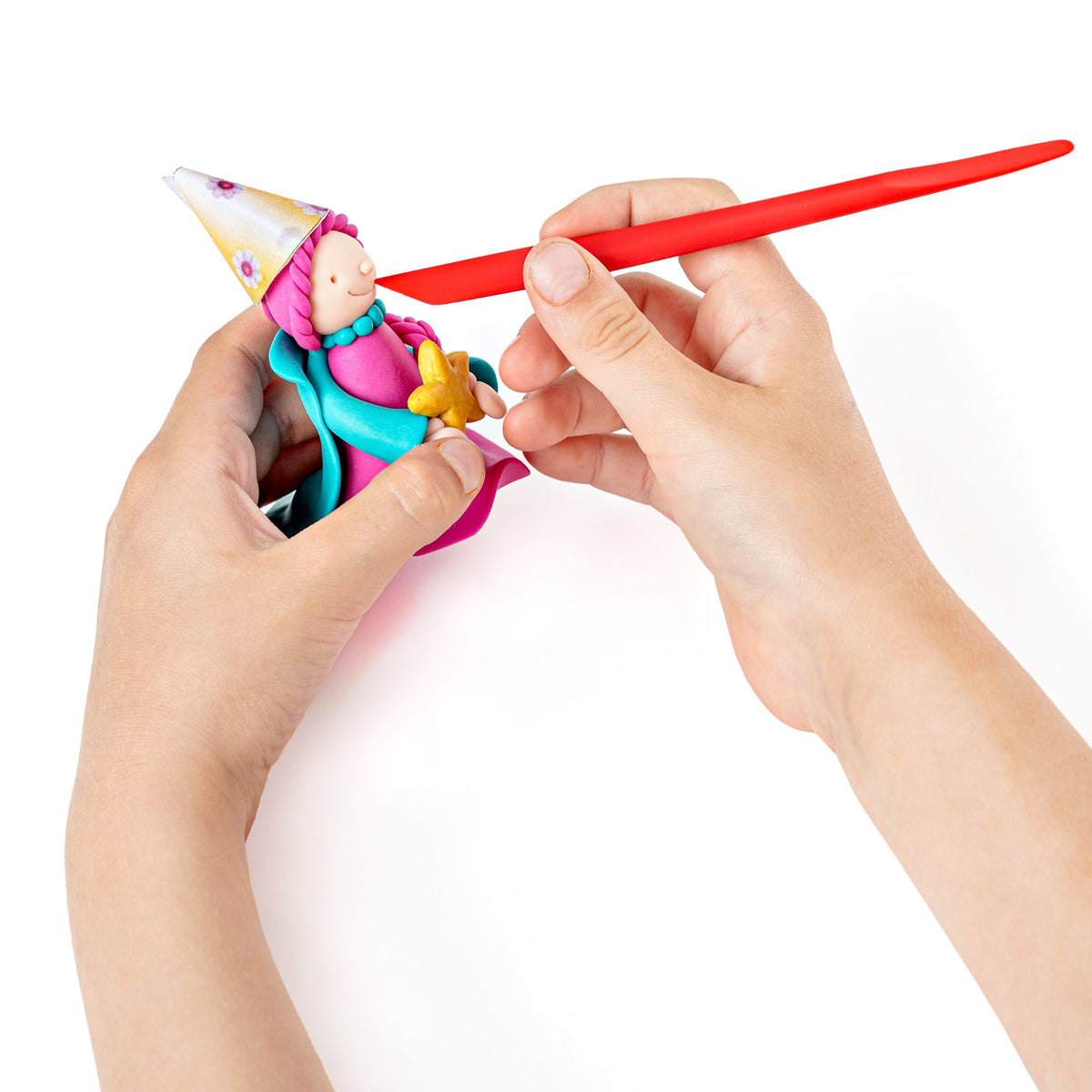 Hands using a red modelling stick to shape the pointed hat of a turquoise and pink clay princess