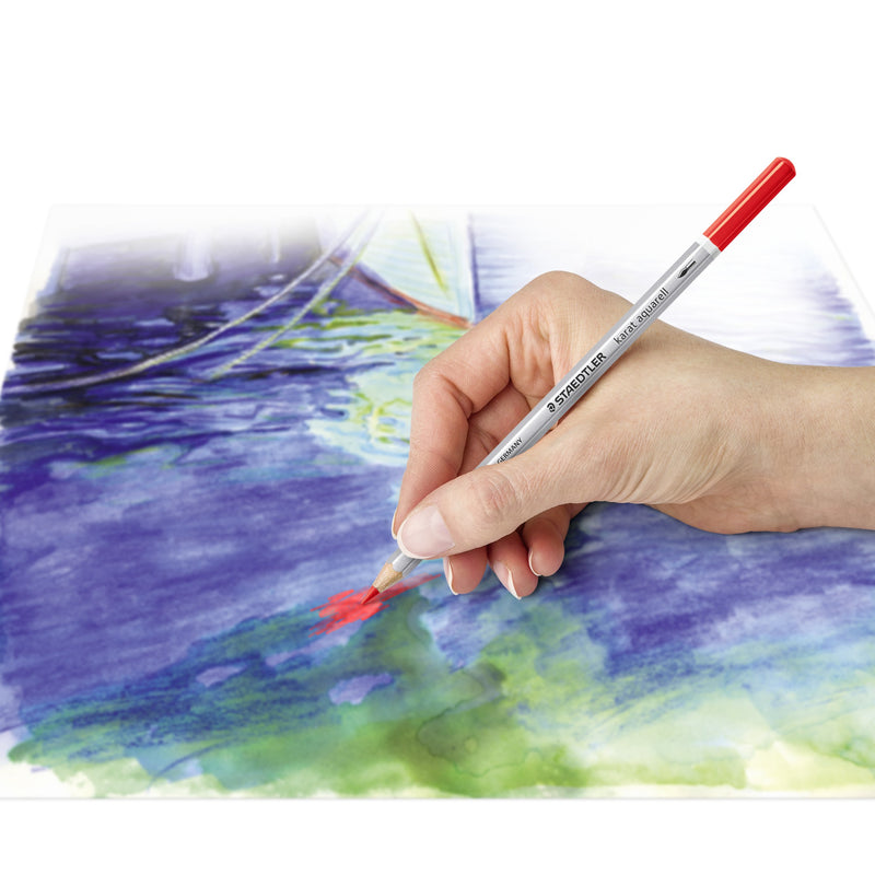 Hand painting a blue water scene with a red karat aquarell pencil, showing washed colour on watercolour paper