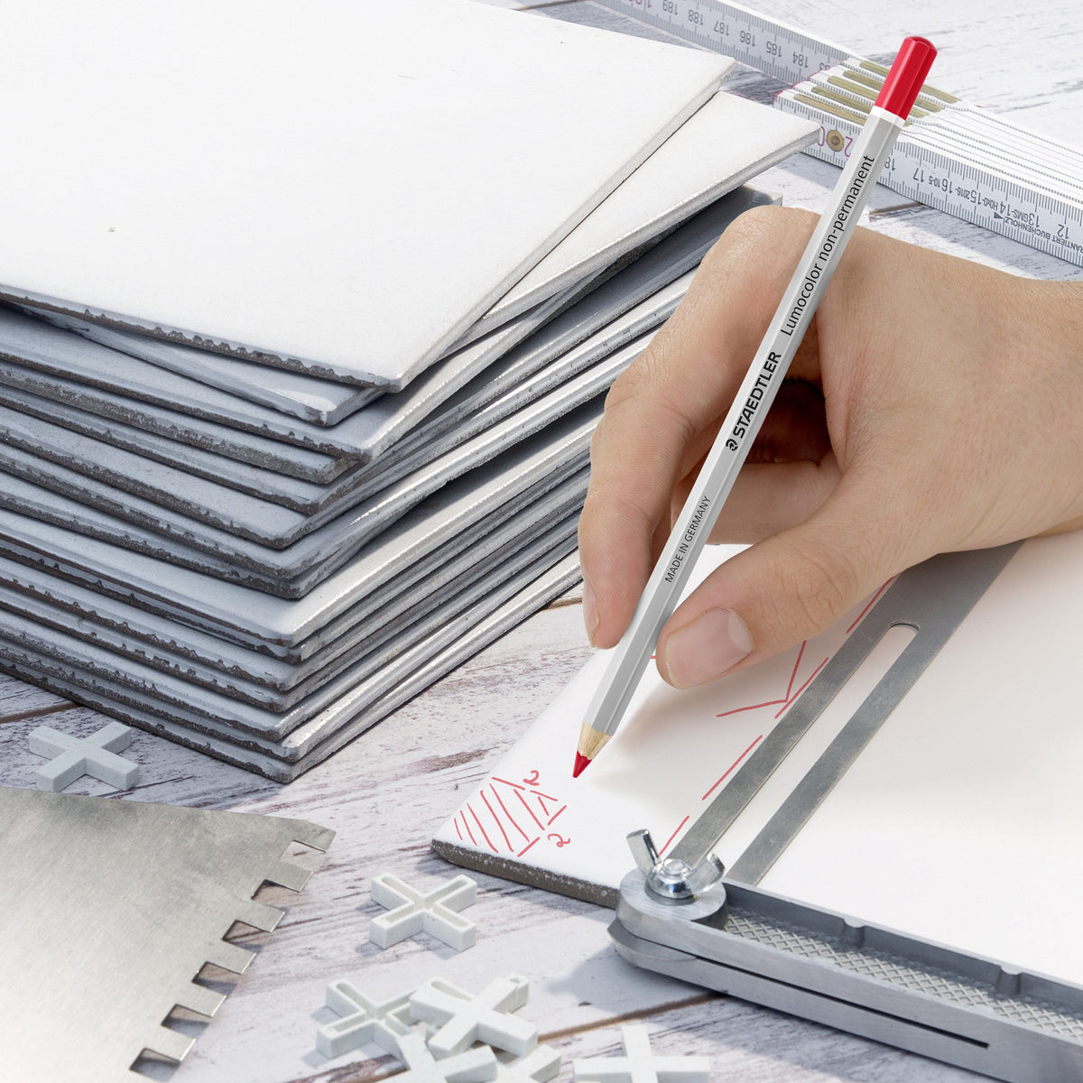 Red omnichrom pencil marking stacked boards against a metal ruler, a hand holding the pencil