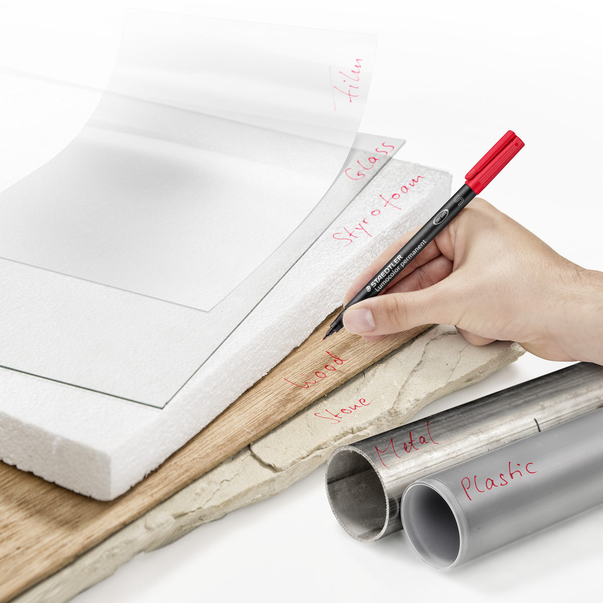 Range application photo of a hand writing on film, glass, wood, stone, metal and plastic with a red superfine Lumocolor