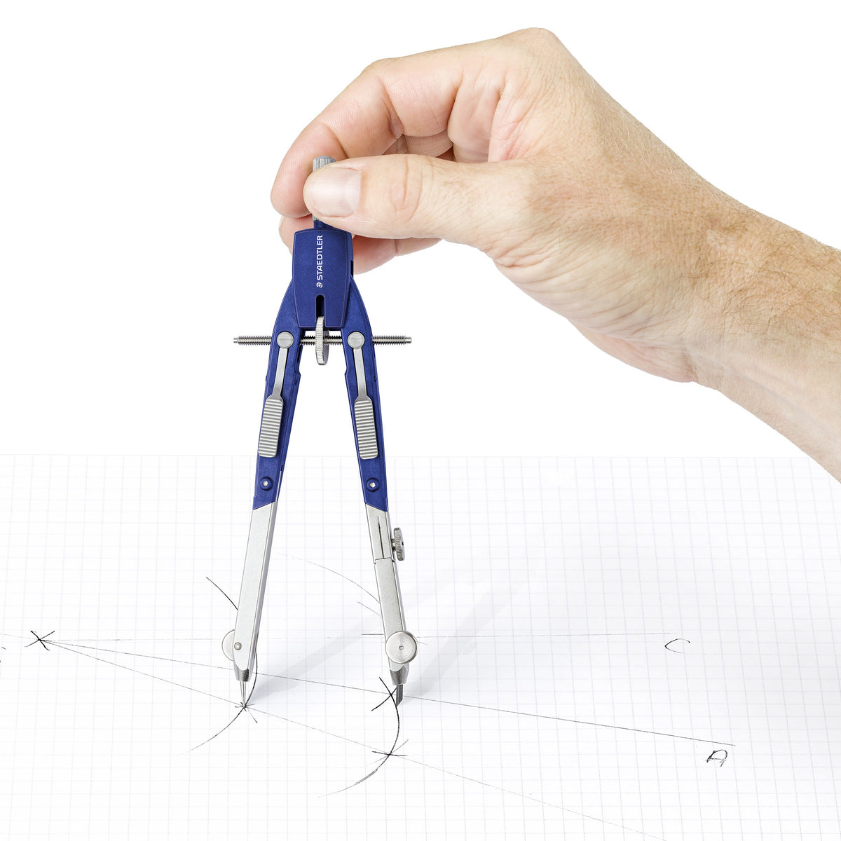 A hand holding the head of the Staedtler 552 compass and drawing circles on squared paper with construction marks