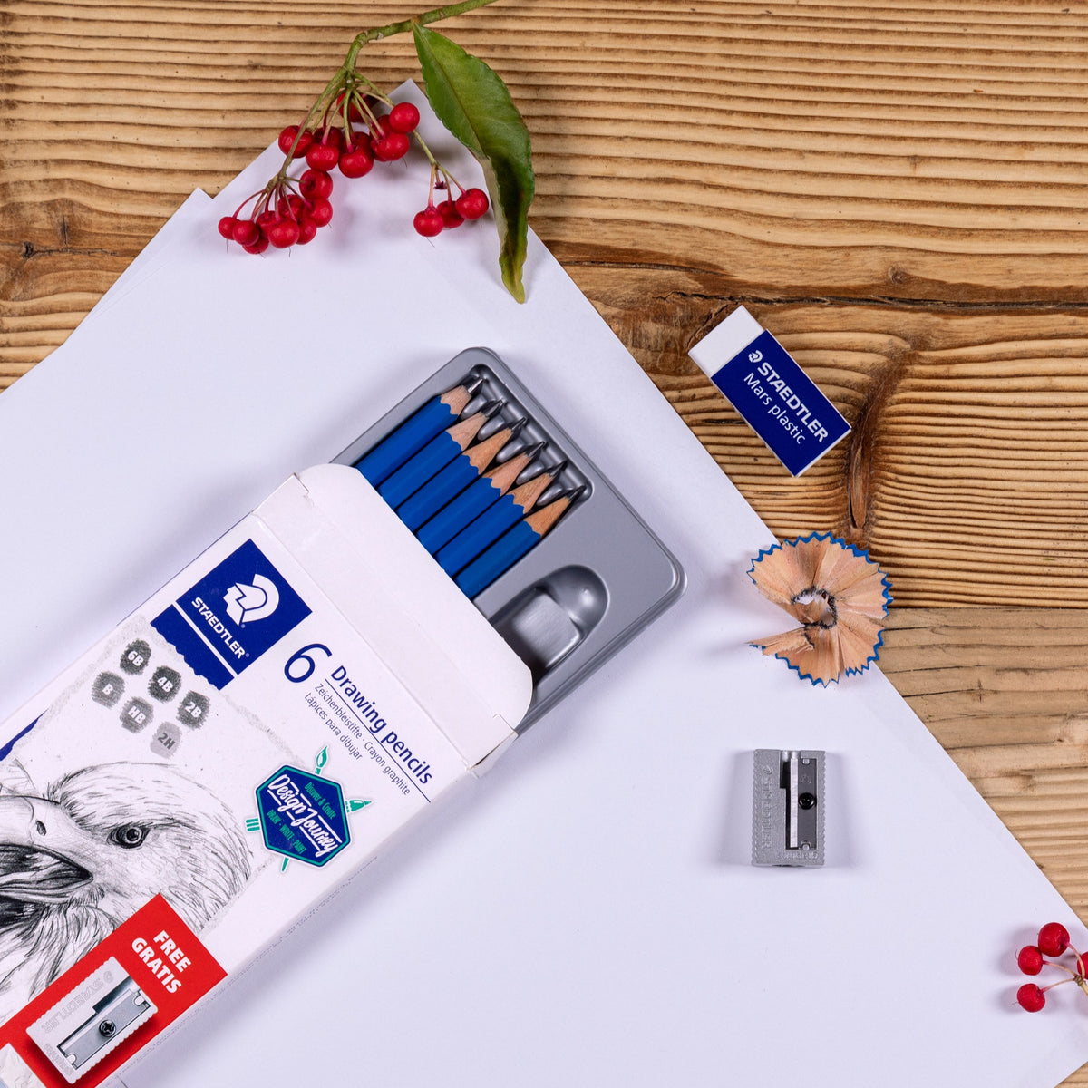 Staedtler Lumograph sketching set opened on a wooden table, six blue pencils in a grey tray beside an eraser, sharpener and shavings