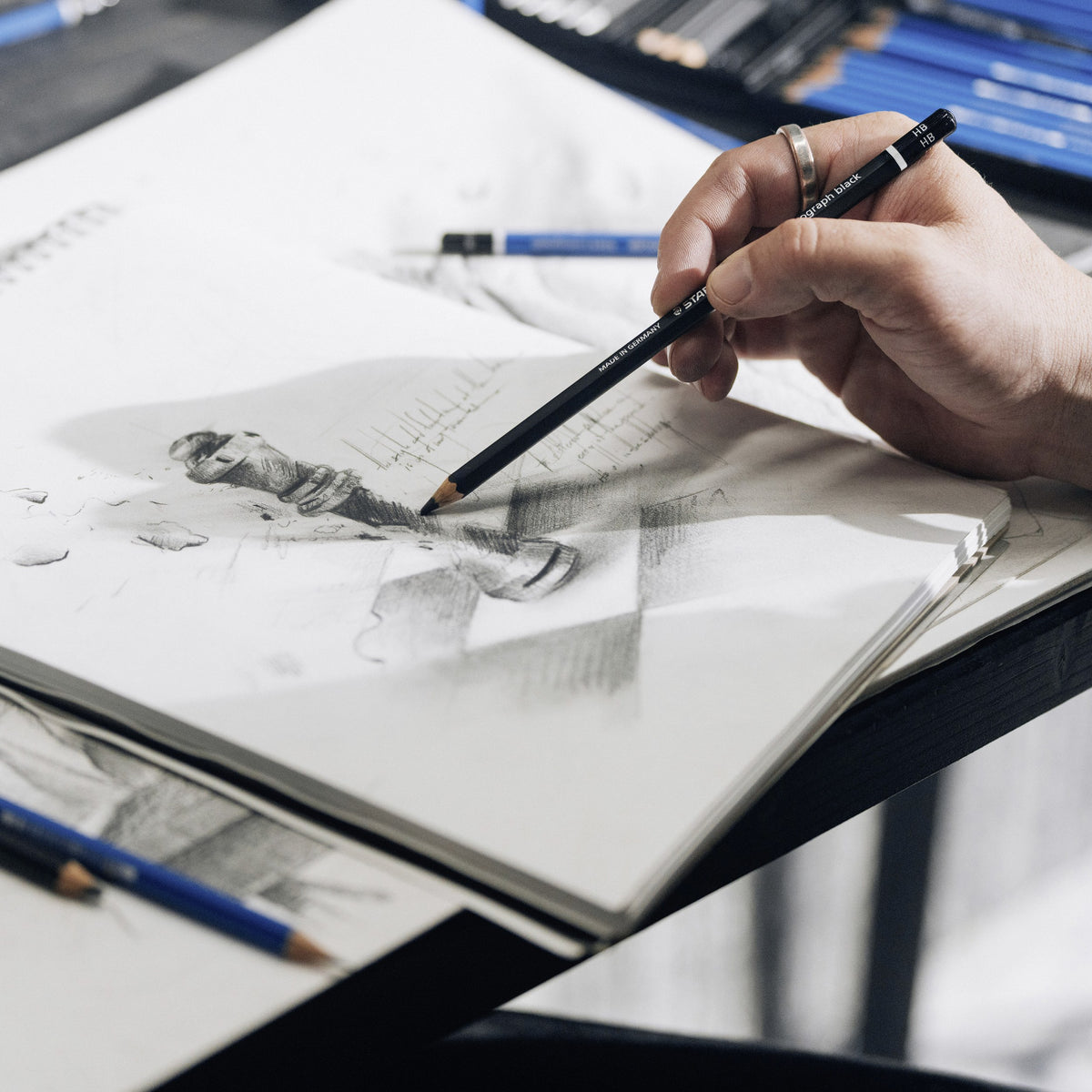 Hand sketching a figure in an open sketchbook with a black Lumograph black pencil, Staedtler photograph