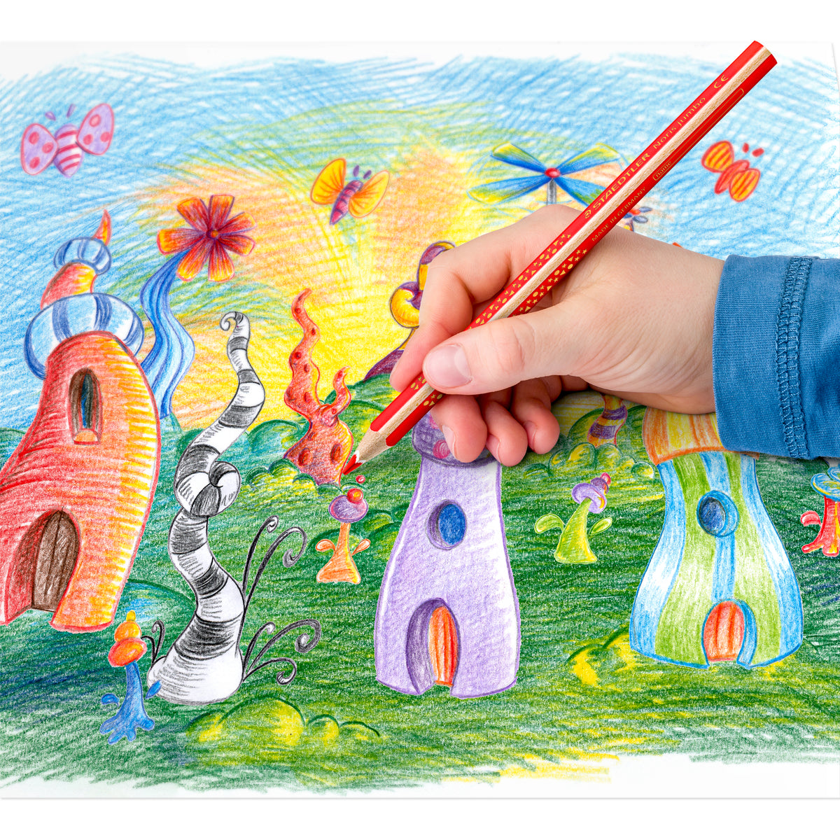 Child colouring a fantasy house drawing with a red Staedtler Noris jumbo triangular coloured pencil