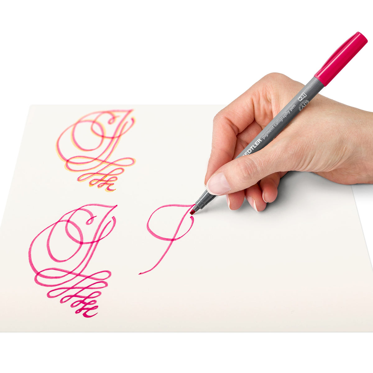 Hand writing pink flourished capital letters with a Staedtler 375 pigment calligraphy pen