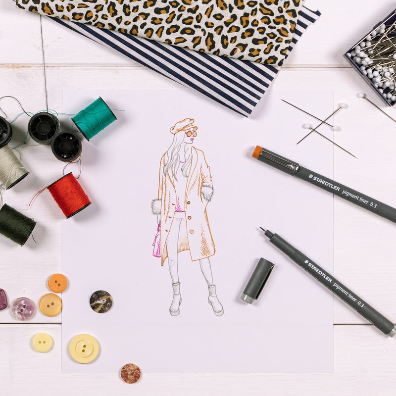 Staedtler photo of a fashion sketch drawn in coloured 0.3 mm pigment liners beside thread spools, buttons and pins