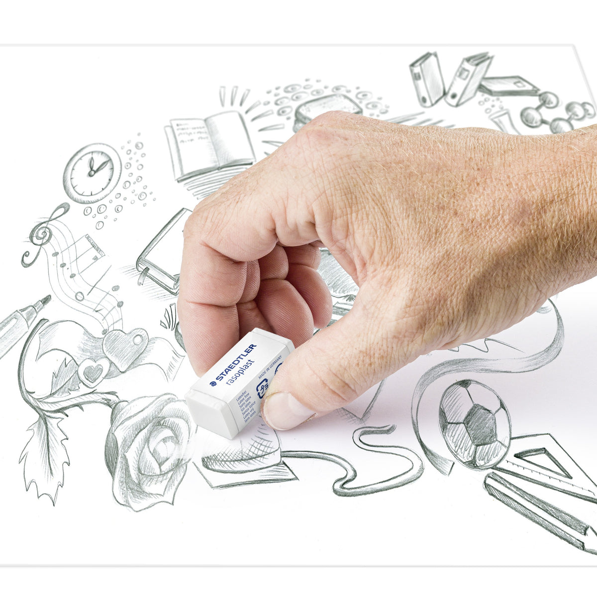 Hand rubbing out pencil lines with a small rasoplast eraser on a sketch of a rose, a clock and a football