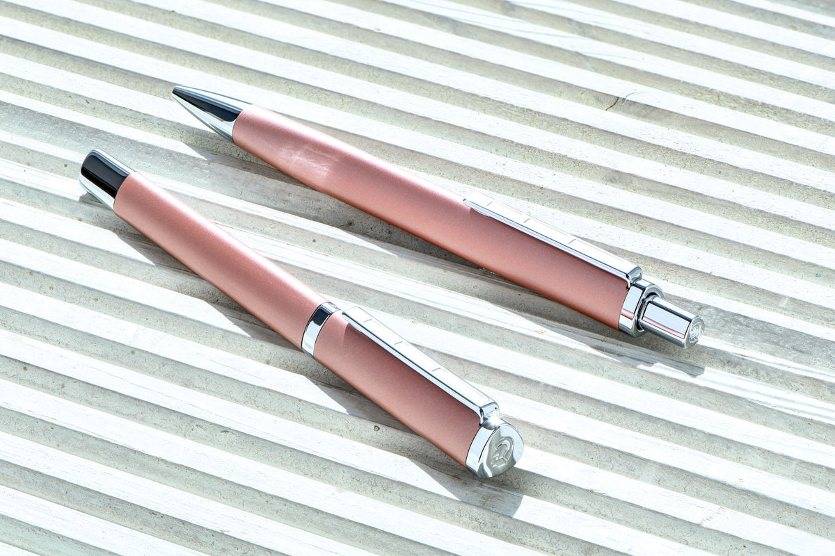 Rose triplus fountain pen and matching rose triplus ballpoint resting on a ridged white surface