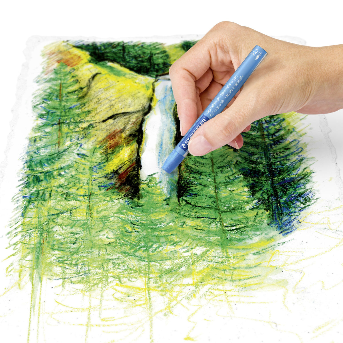 Hand colouring a waterfall and forest scene with a blue Staedtler watercolour crayon, the trees blended into soft green washes