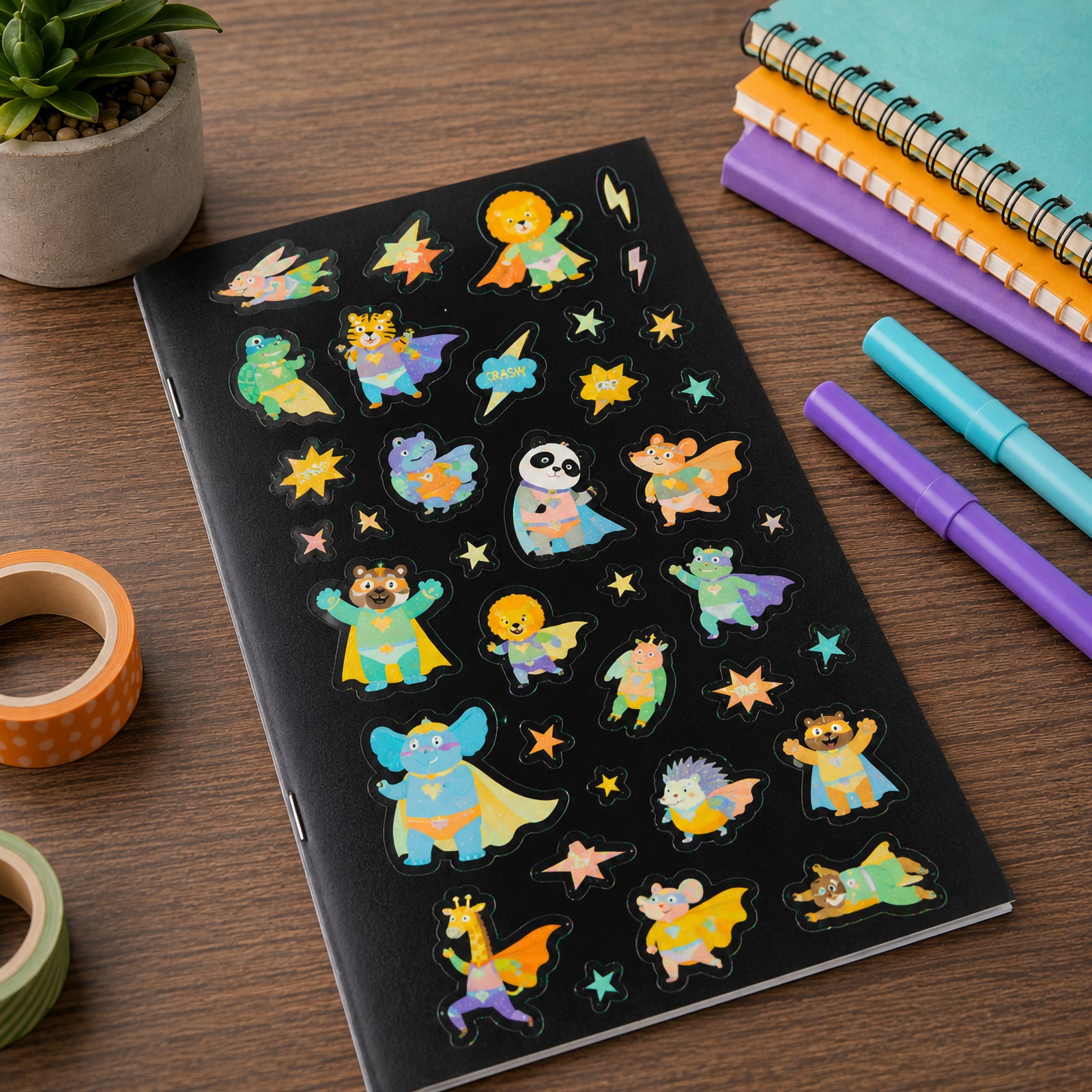 Sticker sheet positioned on a notebook surrounded by stationery supplies. Friendly superhero animals including bears, lions, pandas and elephants appear in colourful capes with action themed stars and comic style elements.