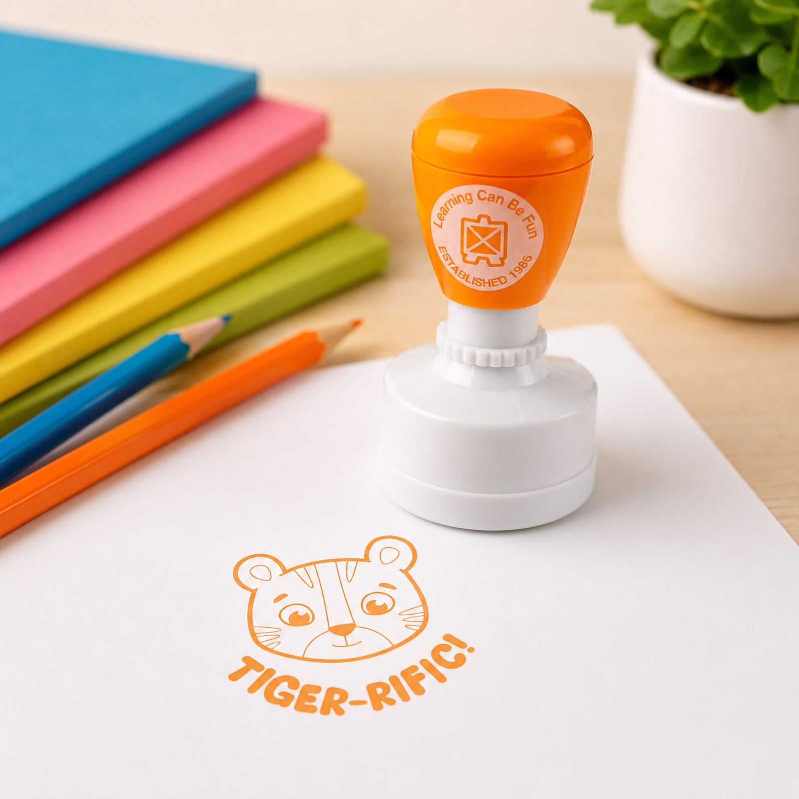 Self inking Tiger-rific Merit Stamp shown with colourful books and pencils in a learning environment. The cheerful tiger design and bold stamp impression demonstrate an engaging way to encourage confidence and celebrate progress.