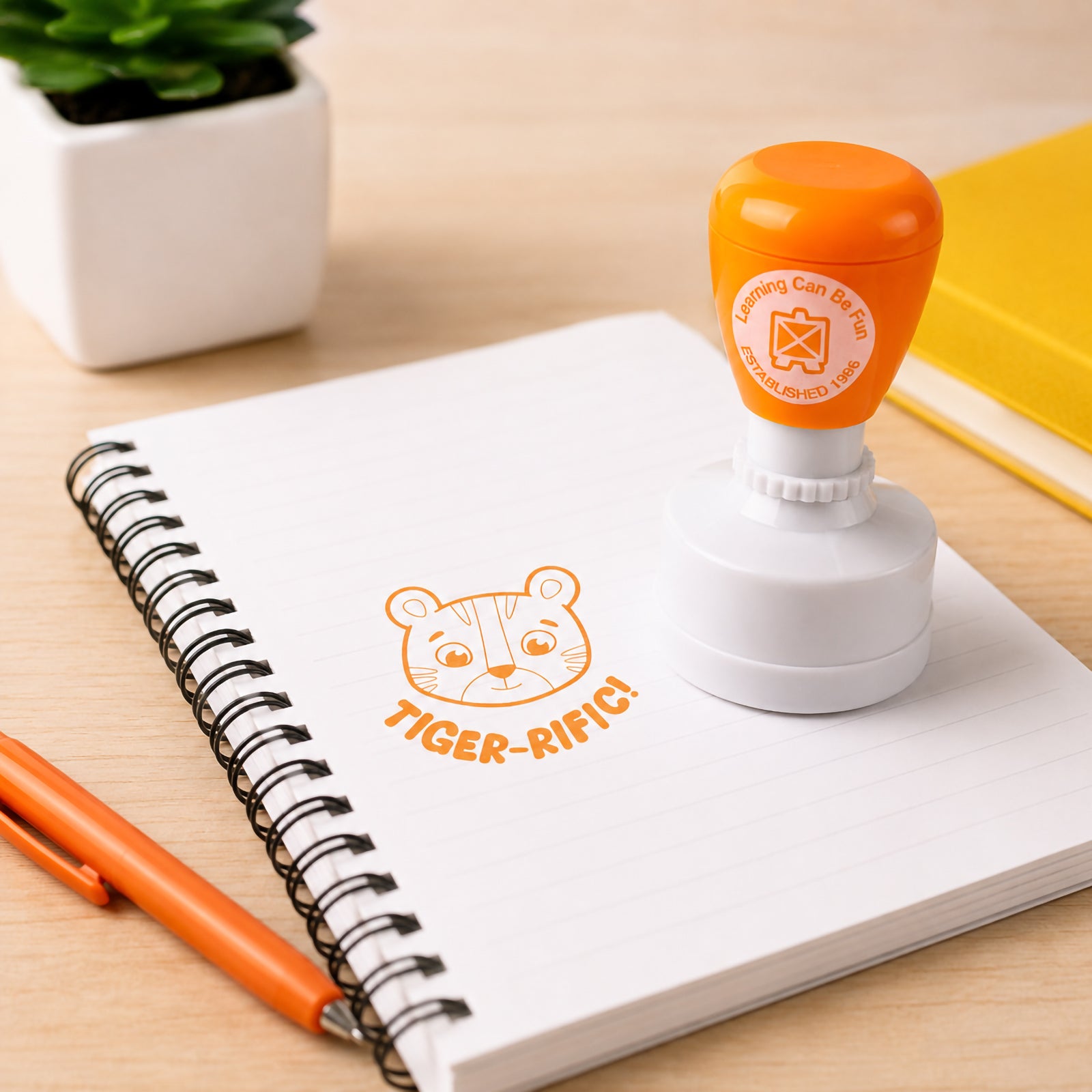 Tiger-rific Merit Stamp positioned on a spiral notebook with a clear tiger face impression and motivational message. The vibrant orange design highlights its suitability for daily classroom feedback, reward programs and positive reinforcement activities.