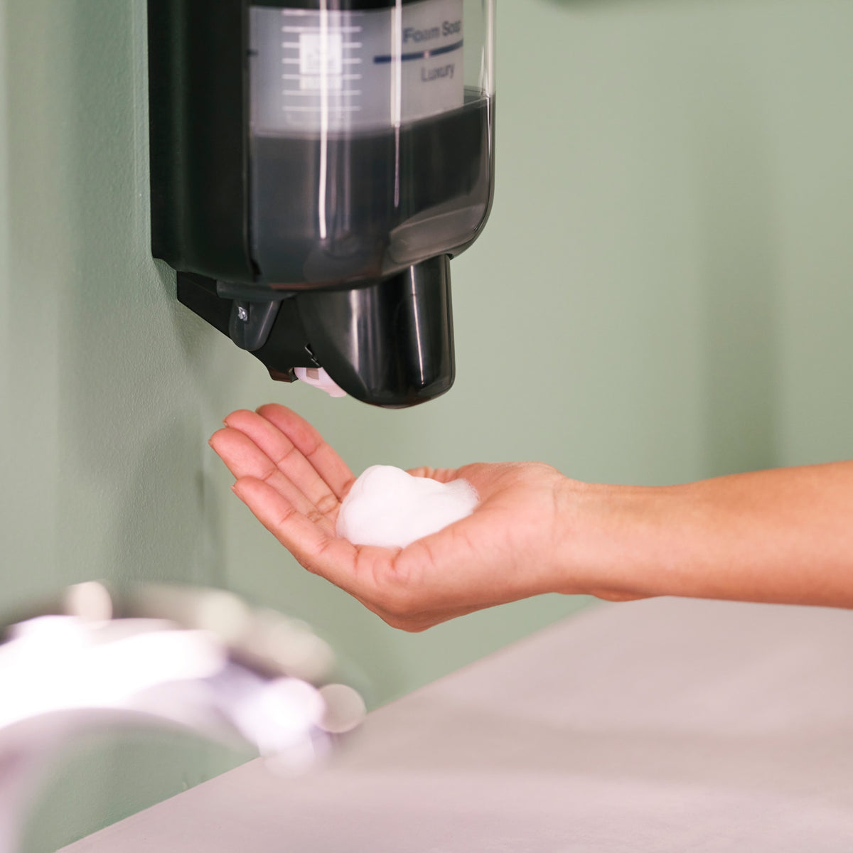 Tork S5 mini dispenser on a washroom wall dispensing foam soap into a hand