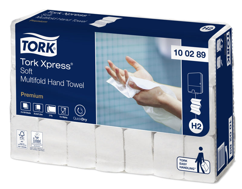Angled view of the clear wrapped Tork Xpress Multifold bundle with white folded towel sleeves visible through the film, label showing 21 x 150 sheets, 25.5 x 21.2 cm, 2 ply, QuickDry and Easy Handling icons.