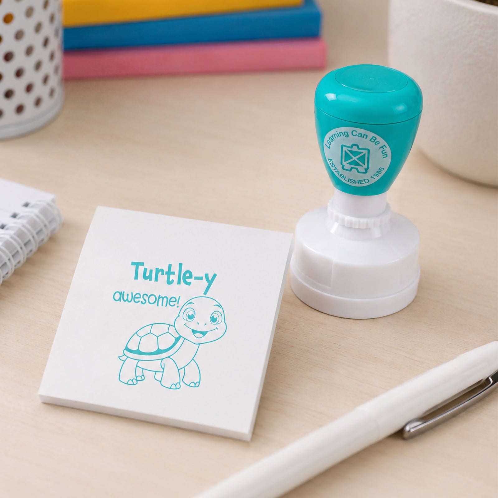 Self inking Turtle-y Awesome Merit Stamp positioned beside a memo pad with a clear turtle impression. The image showcases the compact design and suitability for rewarding classroom participation and learning progress.
