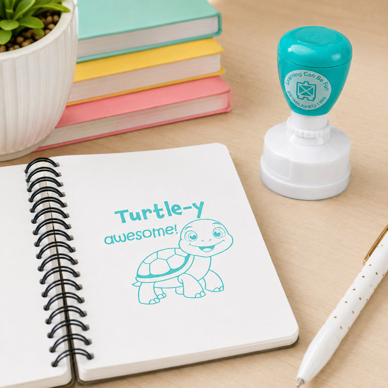 Learning Can Be Fun Turtle-y Awesome Merit Stamp displayed beside an open spiral notebook featuring a bright turtle themed stamp impression. The aqua coloured self inking stamp sits among colourful books and stationery, highlighting its use as a fun classroom reward tool.