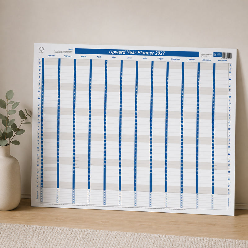 The Upward 2027 Laminated Year Planner is displayed upright against a neutral wall, highlighting its clear year to view layout and reusable laminated finish. The compact wall planner is ideal for keeping project schedules, appointments and annual plans visible in shared workspaces or home offices.