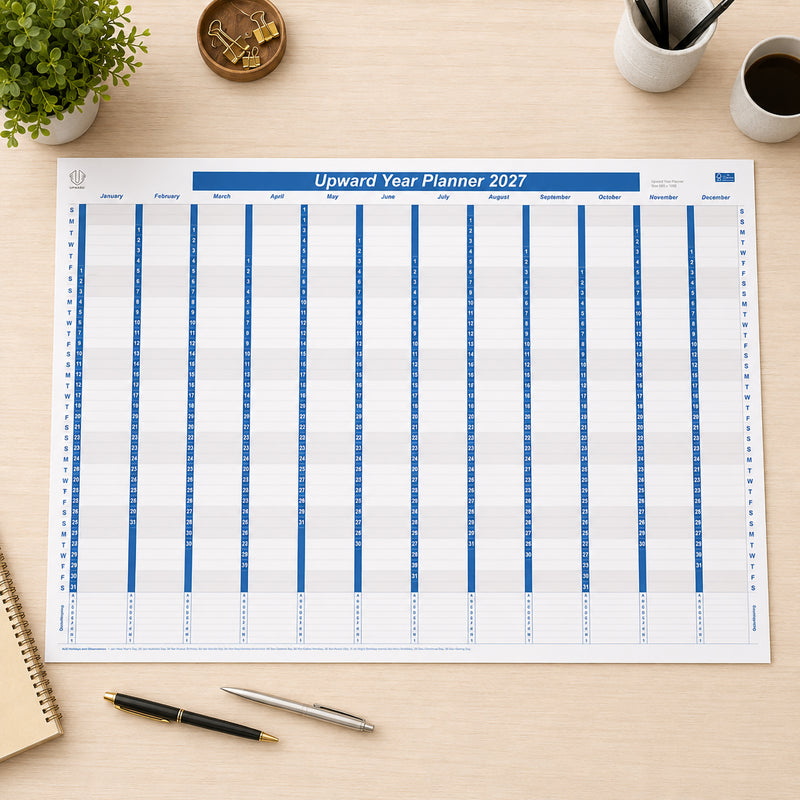 Top view of the Upward 2027 Year Planner laid flat on a clean desk surrounded by office stationery, notebooks and coffee. The large 1005 x 685mm paper planner provides a complete year at a glance, making it ideal for organising business projects, family events and long term schedules.