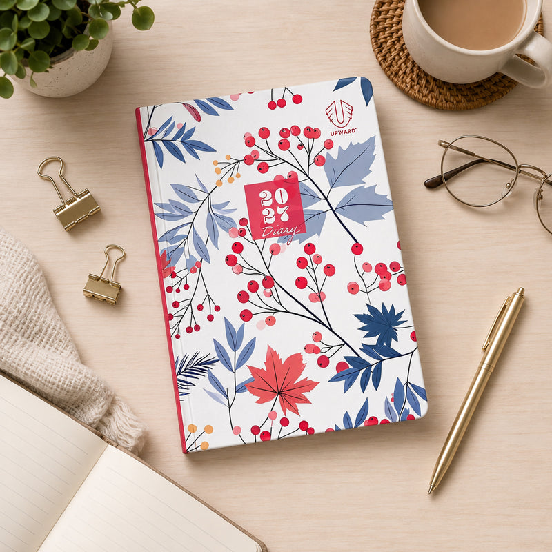 Flat lay workspace featuring the Upward Fashion 2027 A5 Hardcover Week To Opening Diary surrounded by stationery, coffee, glasses and desk accessories, showcasing the colourful Begonia botanical artwork and practical A5 hardcover format for weekly organisation.