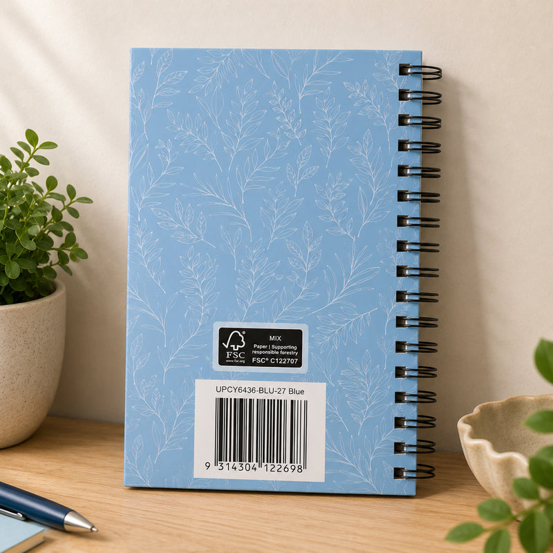 Rear view of the blue hardcover diary standing upright, highlighting the elegant botanical leaf pattern, durable black wire O binding, FSC certification label and product barcode. The premium finish demonstrates a practical diary built for everyday planning throughout the year.