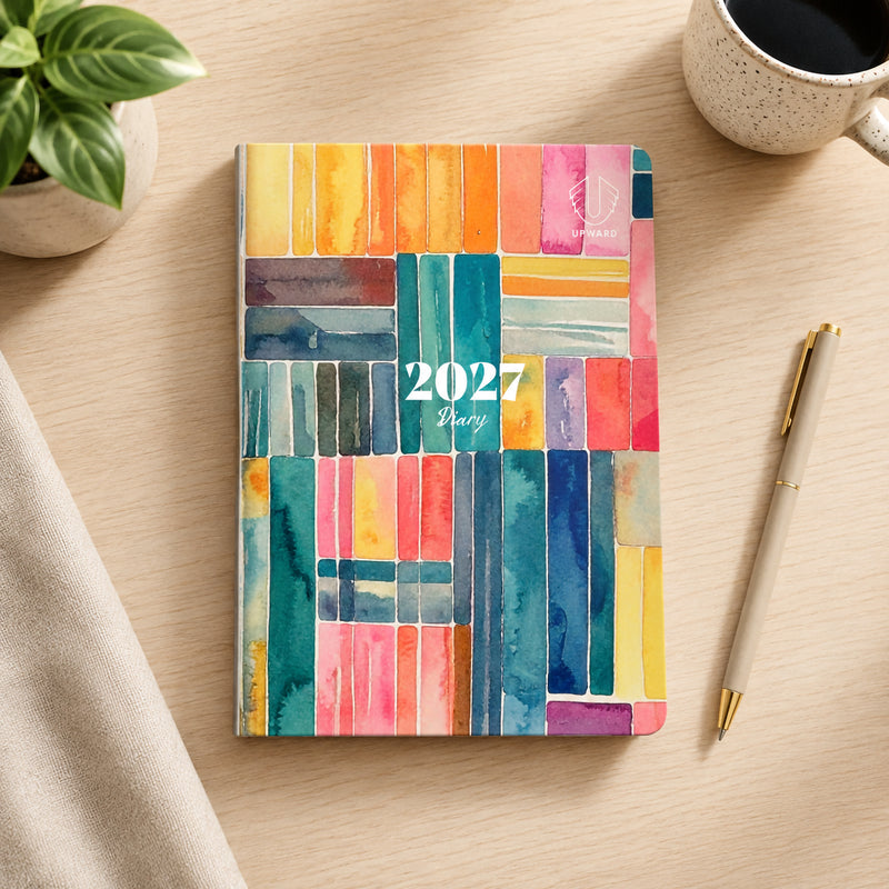 Overhead view of the diary closed on a desk showcasing the colourful Printed Stripe watercolour design. The vibrant combination of blue, pink, orange and yellow tones creates a creative and modern appearance suitable for personal and professional use.