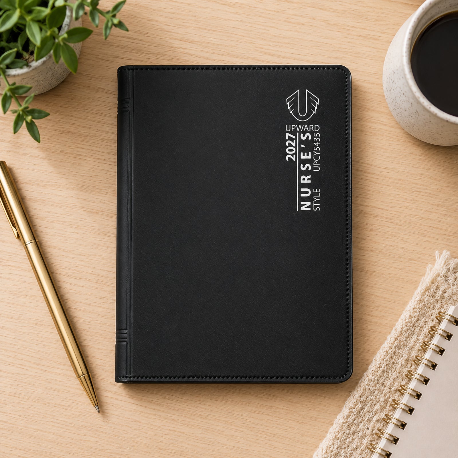 The black Upward Nurse's diary displayed on a desk beside a notebook, coffee cup and pen. Its compact A7 format makes it easy to carry throughout the day while maintaining a professional appearance suitable for healthcare and office environments.