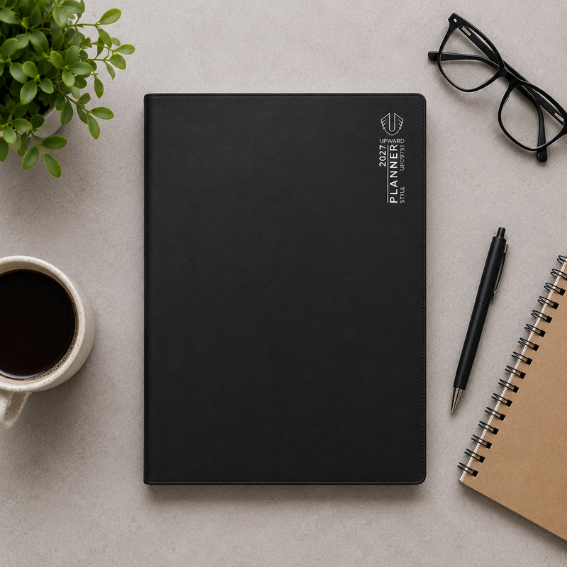 Overhead workspace image showing the Upward Planner 2027 A4 diary with a refined black cover. Positioned beside a notebook, pen, coffee cup and glasses, the planner demonstrates its suitability for business planning, study schedules and daily organisation in a modern workspace.