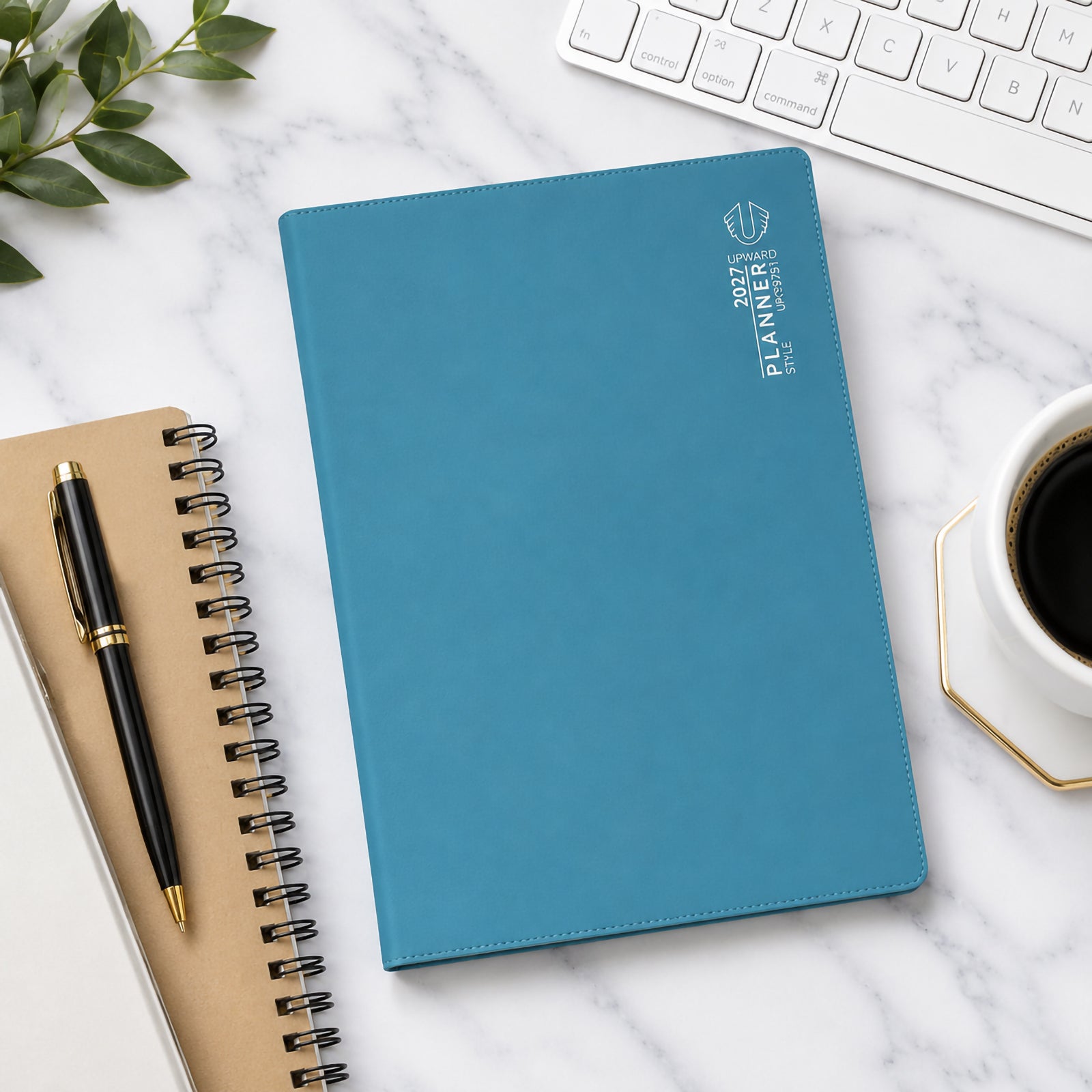 Overhead workspace view showing the Upward Planner 2027 A4 diary with a blue cover placed on a marble desk alongside a keyboard, notebook, coffee cup and pen. The clean design and spacious format make it ideal for business planning, study schedules and personal organisation.
