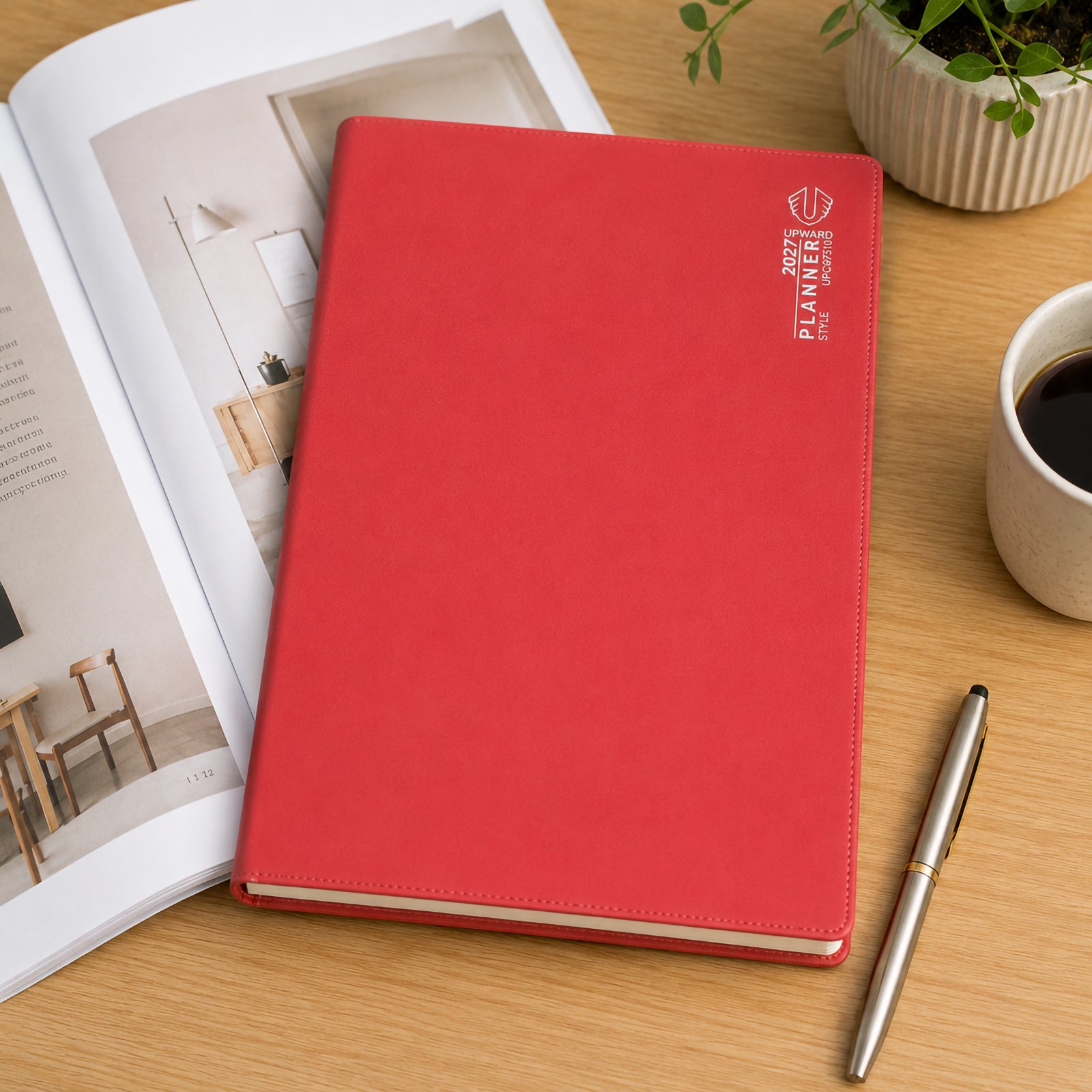 The Upward Planner 2027 A4 diary rests beside an open magazine, coffee cup and premium pen on a modern desk. The bright red cover stands out clearly while showcasing a professional month to view planning format suitable for office, study and home organisation.
