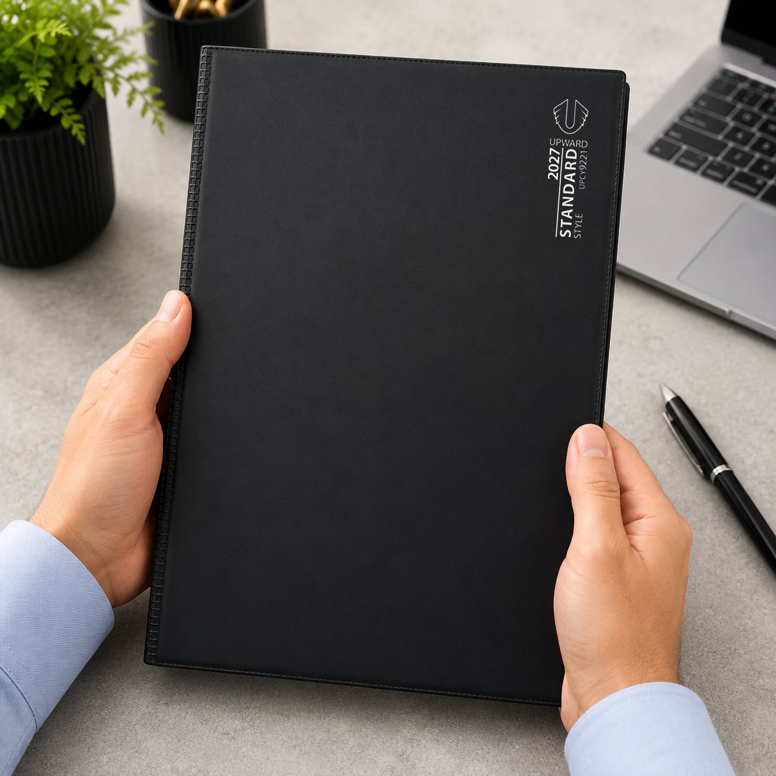 A user holds the Upward Standard 2027 A4 Day To Page Diary, highlighting its large professional format and durable black PVC cover. The generous A4 size is ideal for detailed daily planning, appointments, project tracking and note taking throughout the year.