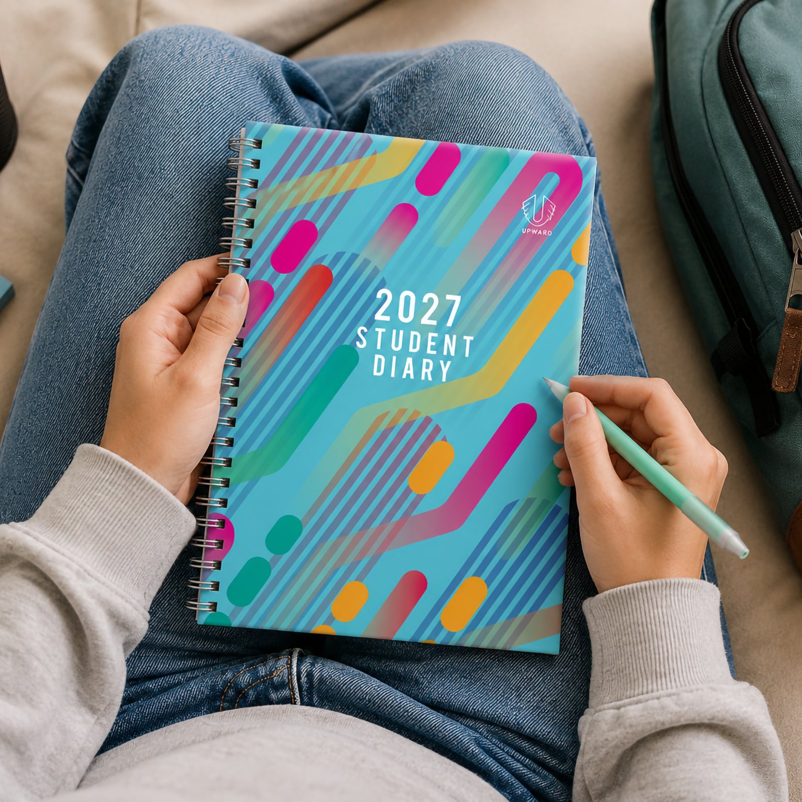A student seated comfortably with the Upward Student 2027 B5 Week To View Diary open on their lap. The vibrant Light Purple cover features colourful abstract shapes and modern graphics, highlighting its student focused design for school planning, homework tracking and daily organisation.