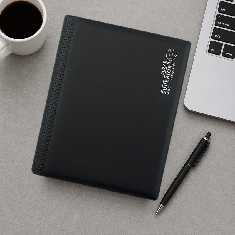 Top down desk view of the Upward Superior 2027 diary placed beside a laptop, coffee cup and pen. The image demonstrates how the diary integrates seamlessly into professional office settings for scheduling meetings, tasks and important deadlines.