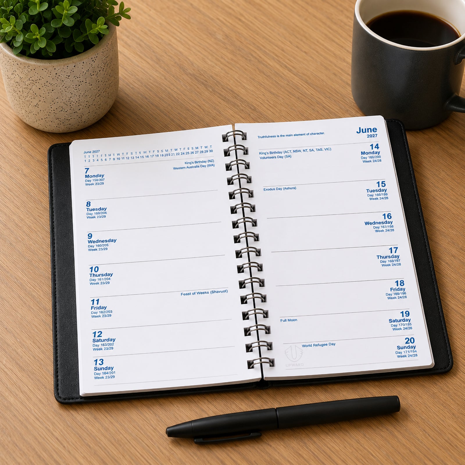 Open Upward Superior 2027 A6/7 Two Week To View Diary displayed on a wooden desk beside a coffee cup and pen. The extended planning layout shows two full weeks across the spread, providing ample space for appointments, reminders and long term scheduling.