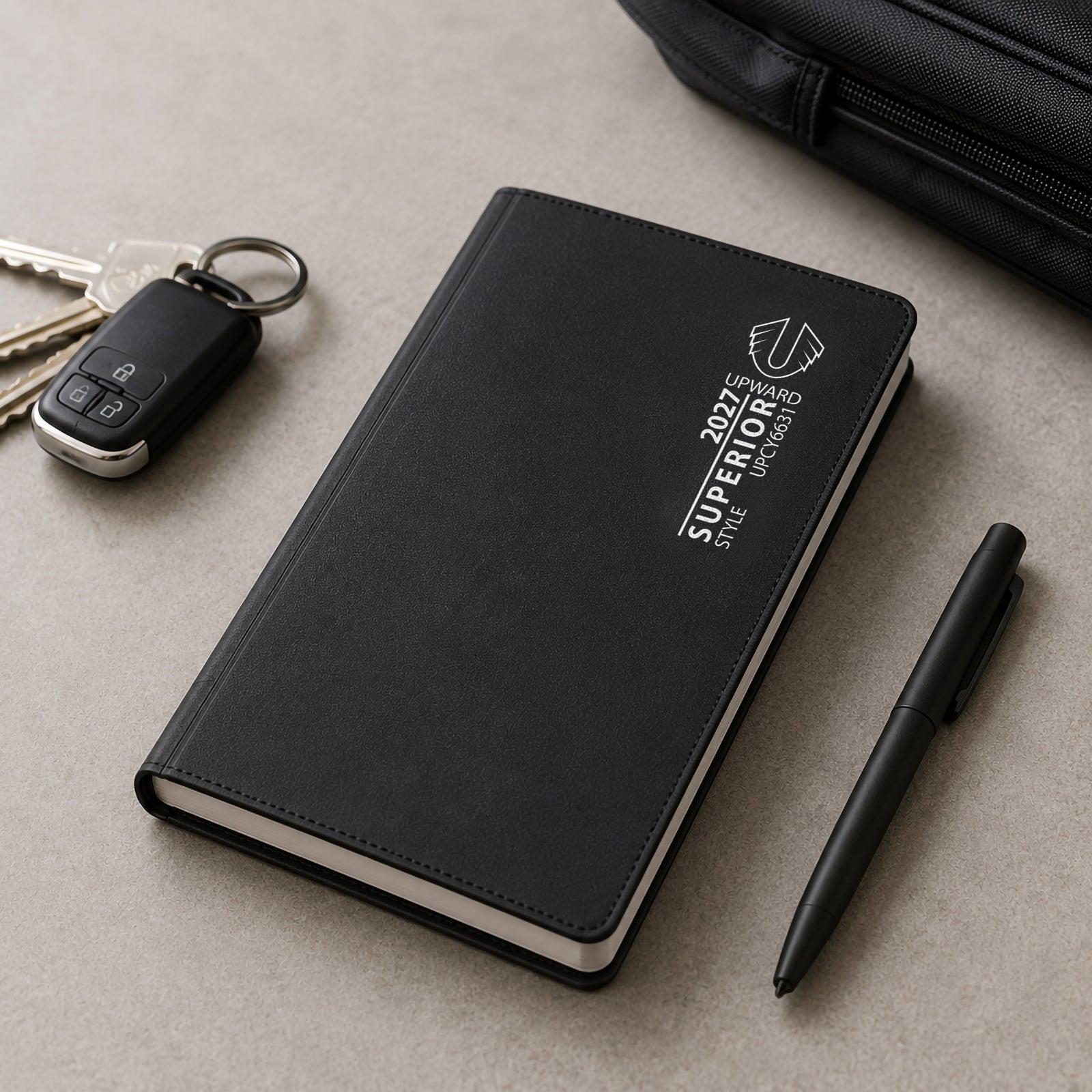 Closed Upward Superior 2027 diary positioned beside keys, a pen and travel accessories. The image highlights the compact portable design and durable black PVC cover, making it suitable for daily commuting and business use.