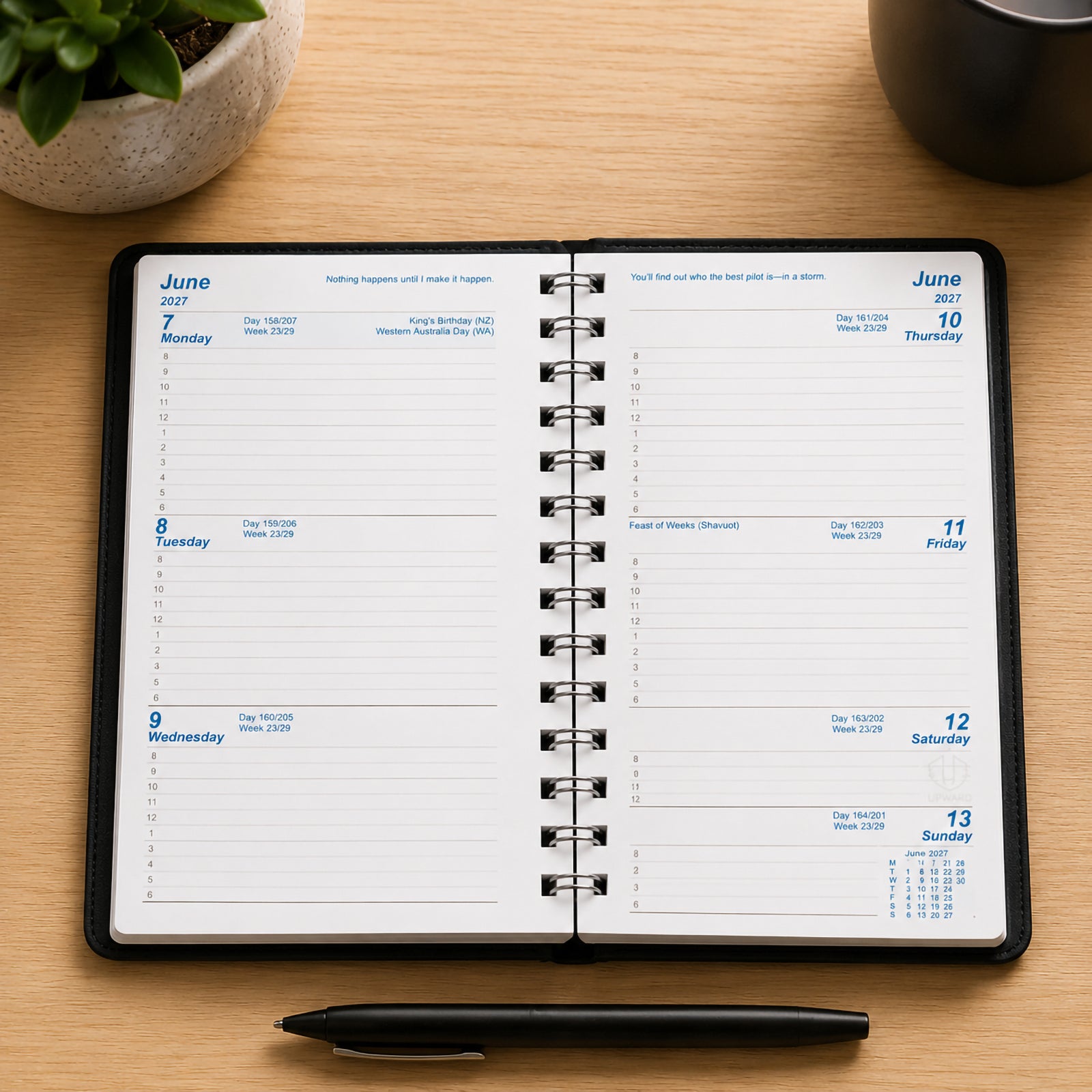 Open Upward Superior 2027 A6/7 Week To View Diary displayed on a timber desk with a pen and decorative plant. The internal layout shows a full weekly planning spread with ample writing space for appointments, reminders, meetings and daily schedules.