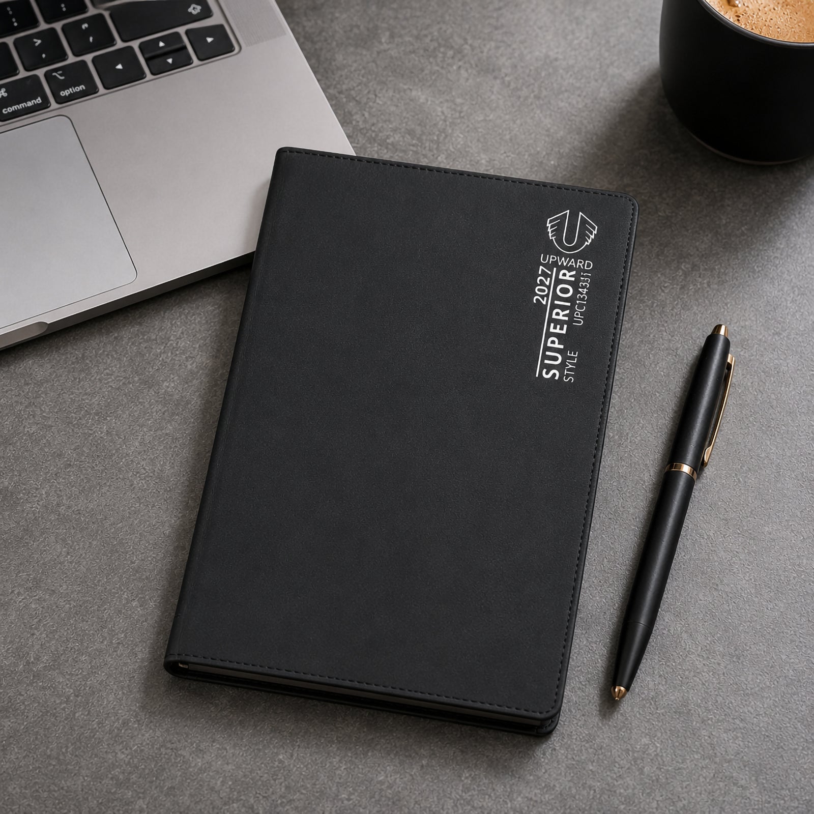 The Upward Superior 2027 diary featuring a sleek black PVC cover resting beside a laptop, coffee cup and premium pen. The compact B6 format highlights its portability, making it suitable for professionals who need organised scheduling while working in the office or on the move.