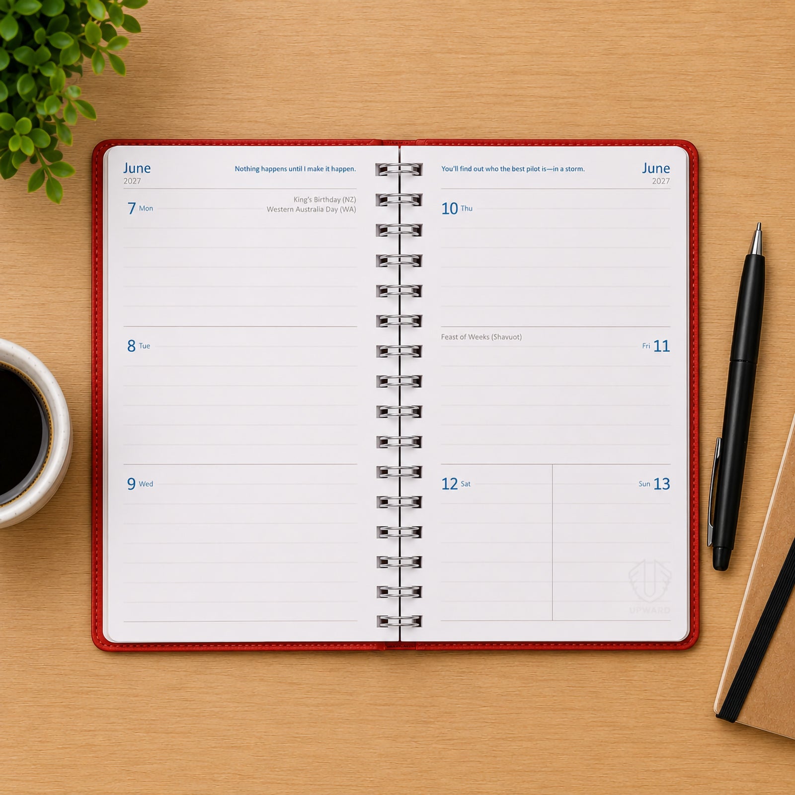 Open view of the Upward Superior 2027 B6 Week To View Diary showing a full weekly layout across two pages. The diary sits on a timber desk beside a coffee cup, pen, notebook and decorative plant, demonstrating ample writing space for appointments, reminders, deadlines and weekly planning.