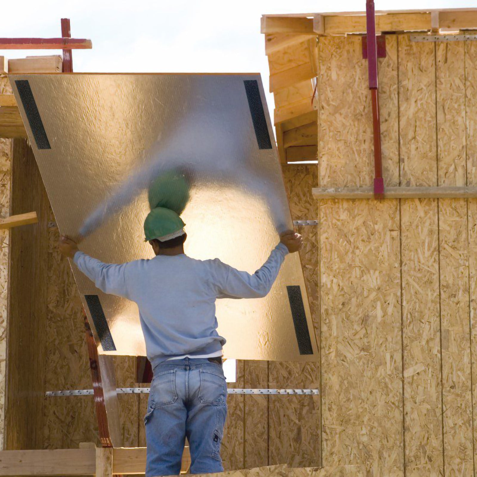 Construction worker positioning a large insulated board secured with black heavy duty Velcro fastening strips. The image demonstrates industrial strength holding power for demanding building and installation projects.