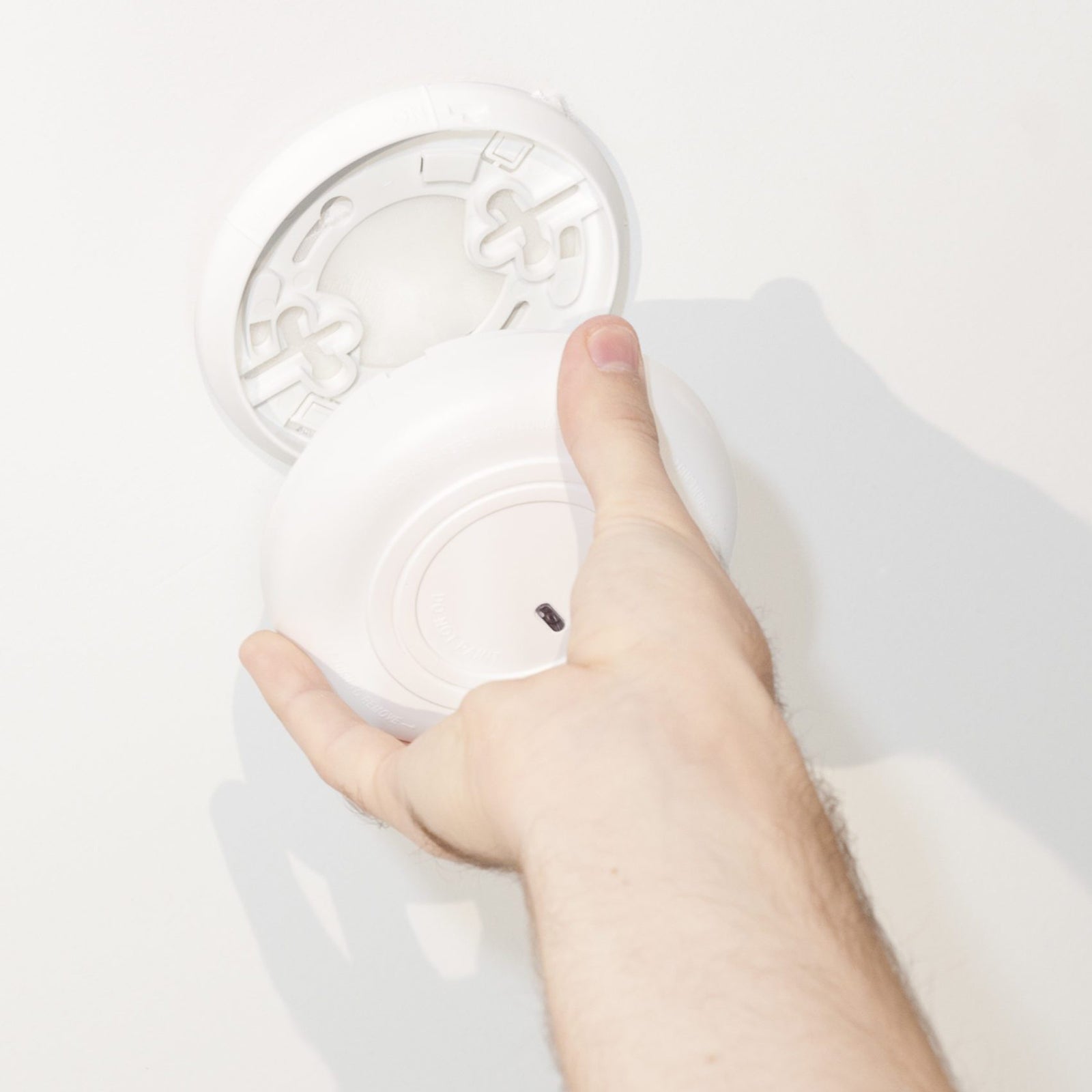 A close up shows a hand attaching a white round item to a wall mounted base using heavy duty hook and loop fastening. The image demonstrates the tape being used for clean, secure wall mounting on a smooth white surface.