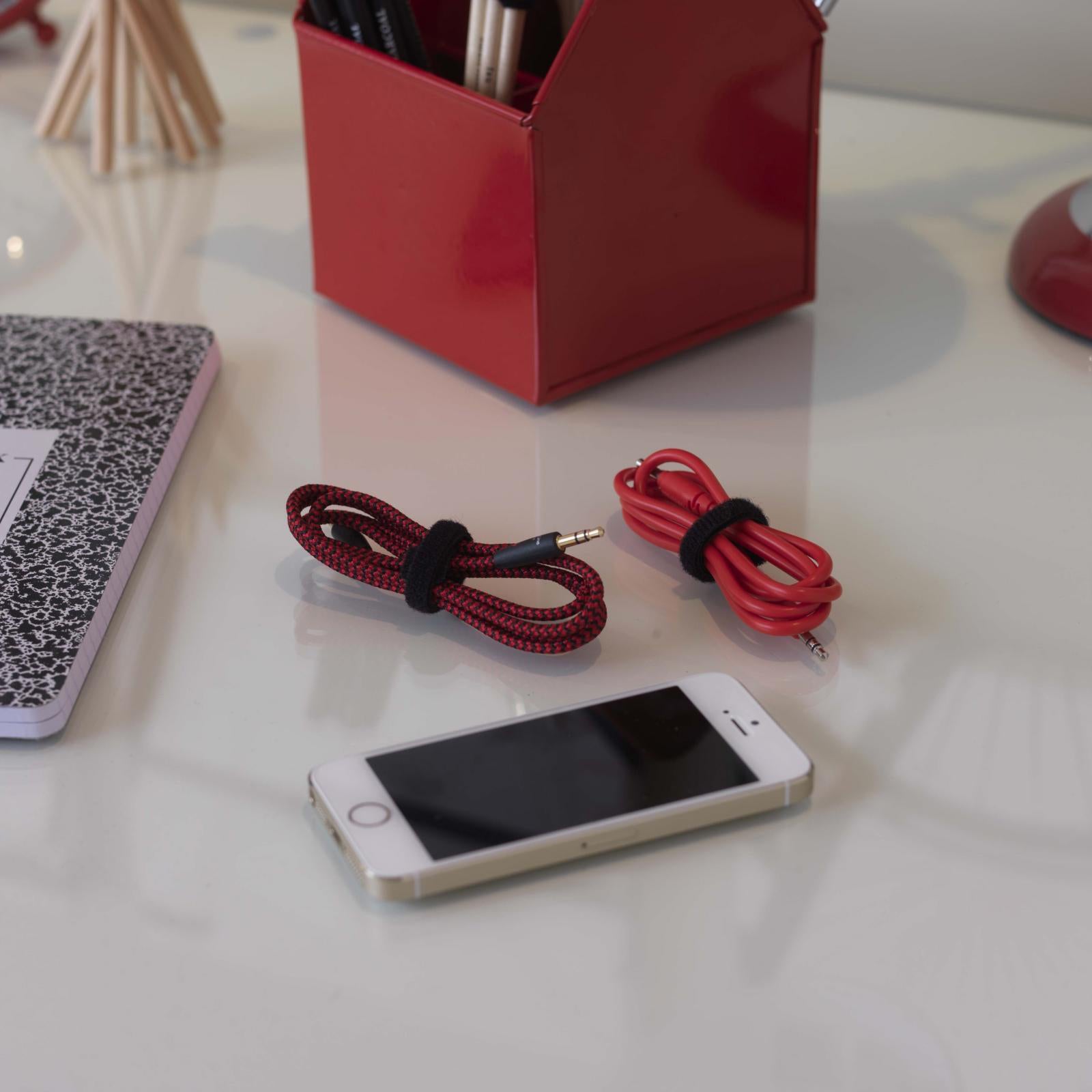 Organised desktop setup featuring bundled audio and charging cables secured neatly with black VELCRO Brand ONE WRAP reusable cable ties beside a smartphone and office accessories.