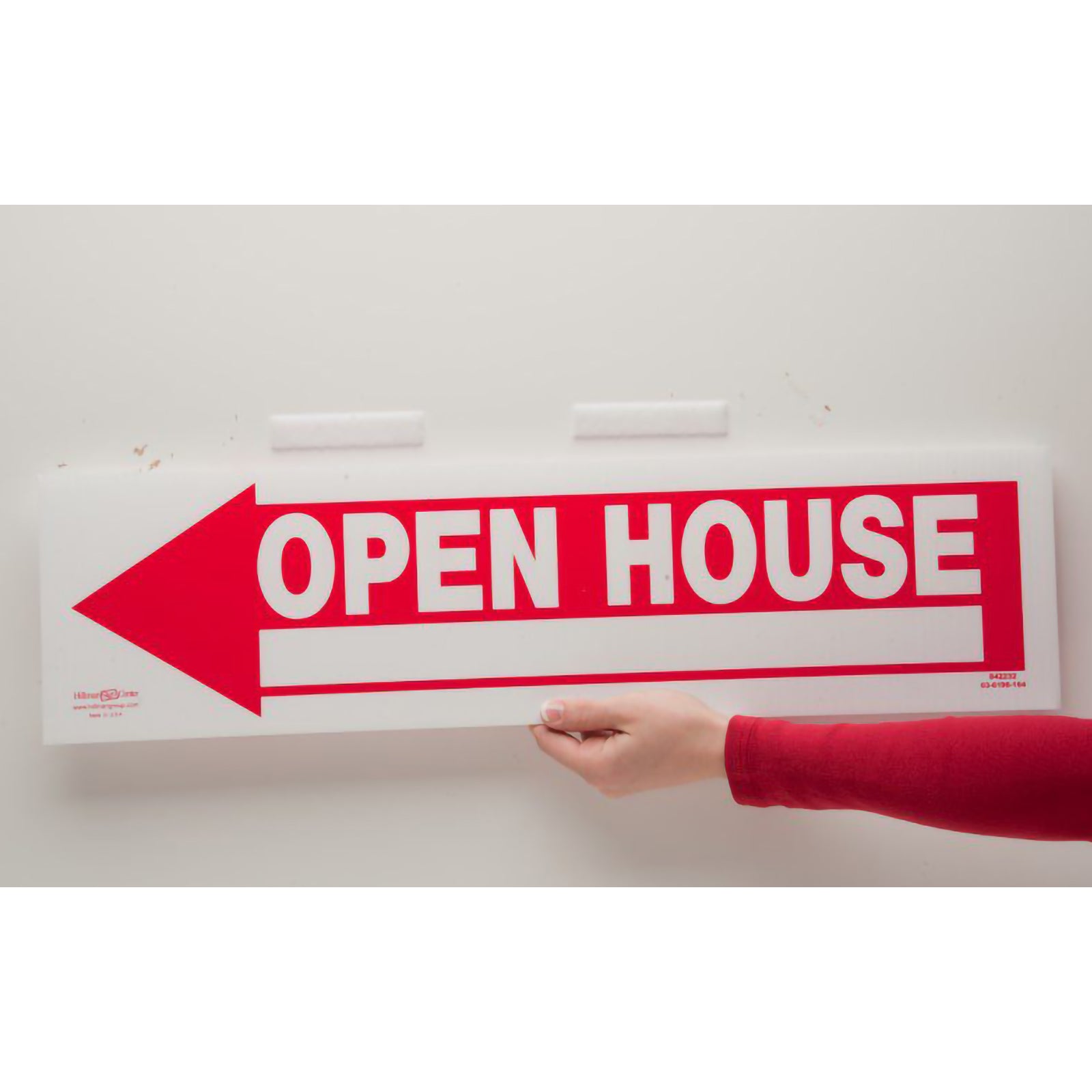 A large open house sign is being mounted onto a smooth wall using white Velcro stick on tape. The image demonstrates removable indoor fastening for signage, displays and lightweight mounting applications.