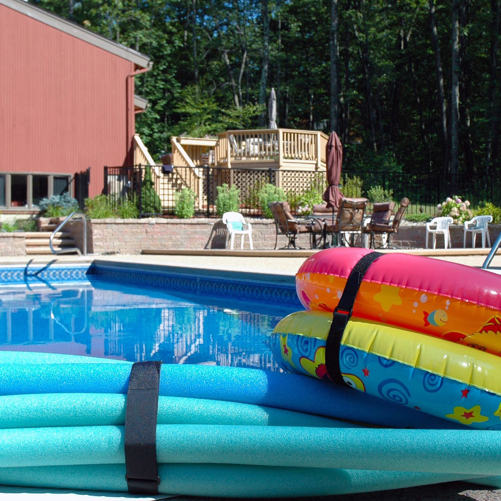 Poolside scene showing colourful inflatable pool rings and foam pool noodles bundled securely together using black VELCRO Brand VELSTRAP adjustable straps.