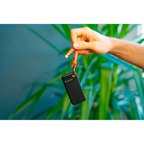 Verbatim Pocket SSD hanging from its orange cable loop held in a hand against green leaves