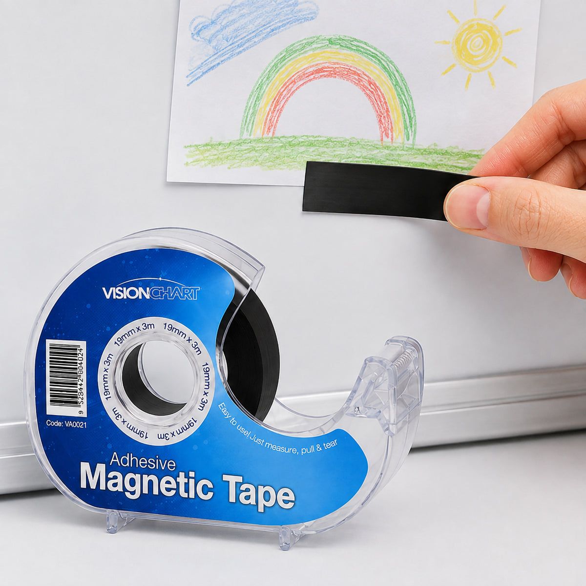 A hand applies a strip of Visionchart self adhesive magnetic tape to the back of a child's drawing before attaching it to a magnetic whiteboard. The image demonstrates the tape's simple peel and stick application for displaying artwork and lightweight documents.