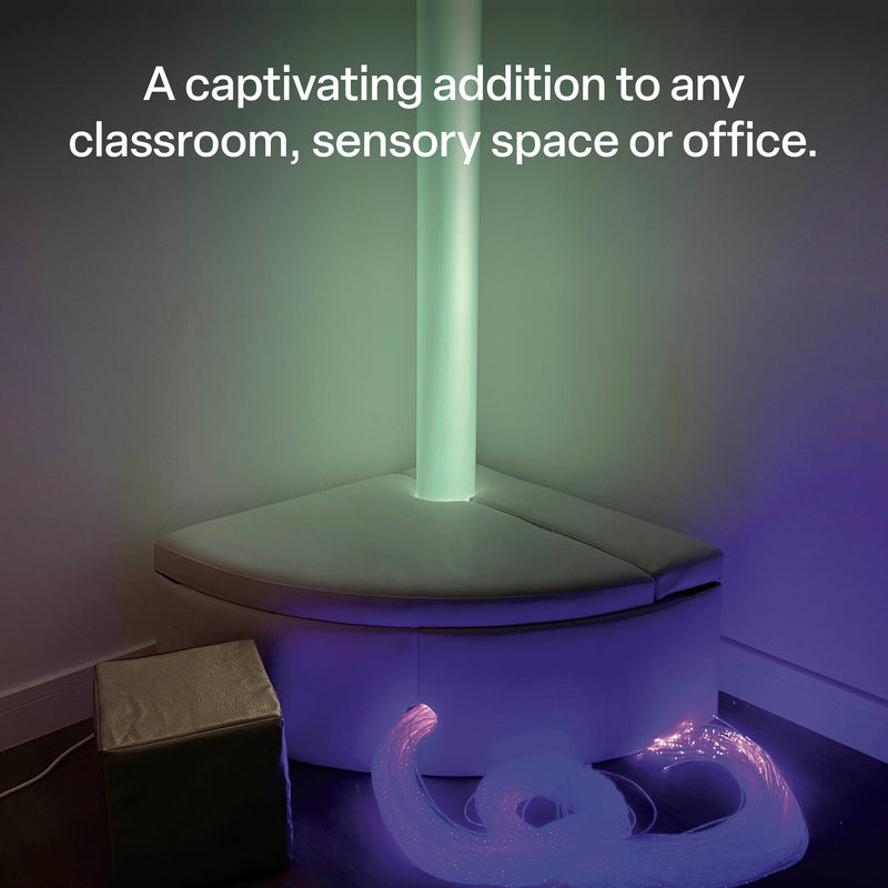 Waterless LED sensory tube installed in a sensory environment with soft surrounding equipment and fibre optic resources. The illuminated tube creates a gentle green glow across the nearby walls, demonstrating how the tall light feature can become a visually captivating addition to classrooms, sensory spaces and other supervised indoor environments.