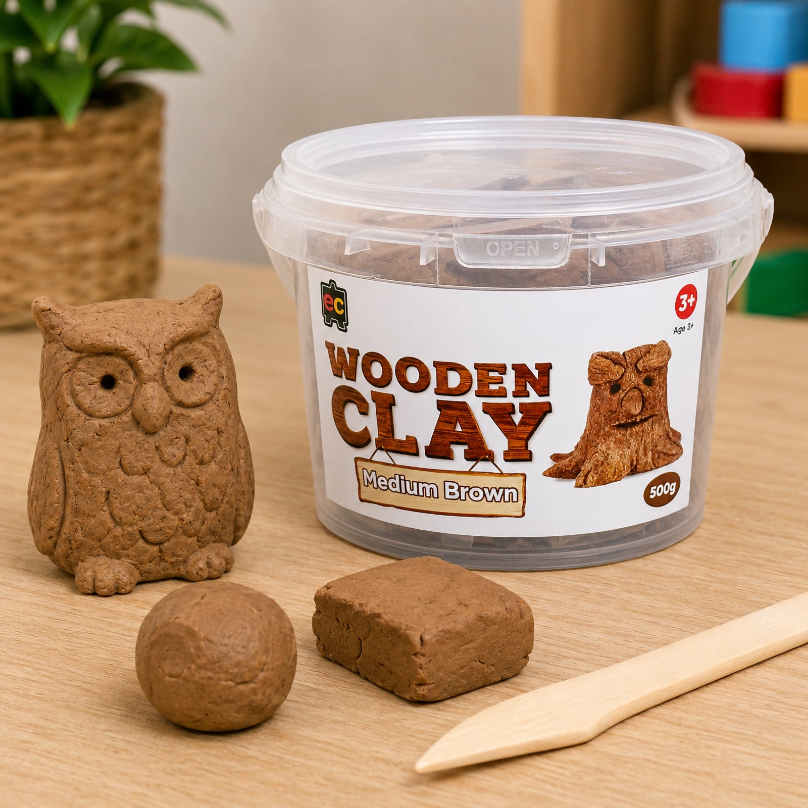 Wooden Clay 500g Medium Brown tub displayed beside a handcrafted owl sculpture and clay blocks on a wooden craft table. The image showcases the clay's natural earthy colour and textured finish suitable for creative modelling activities.